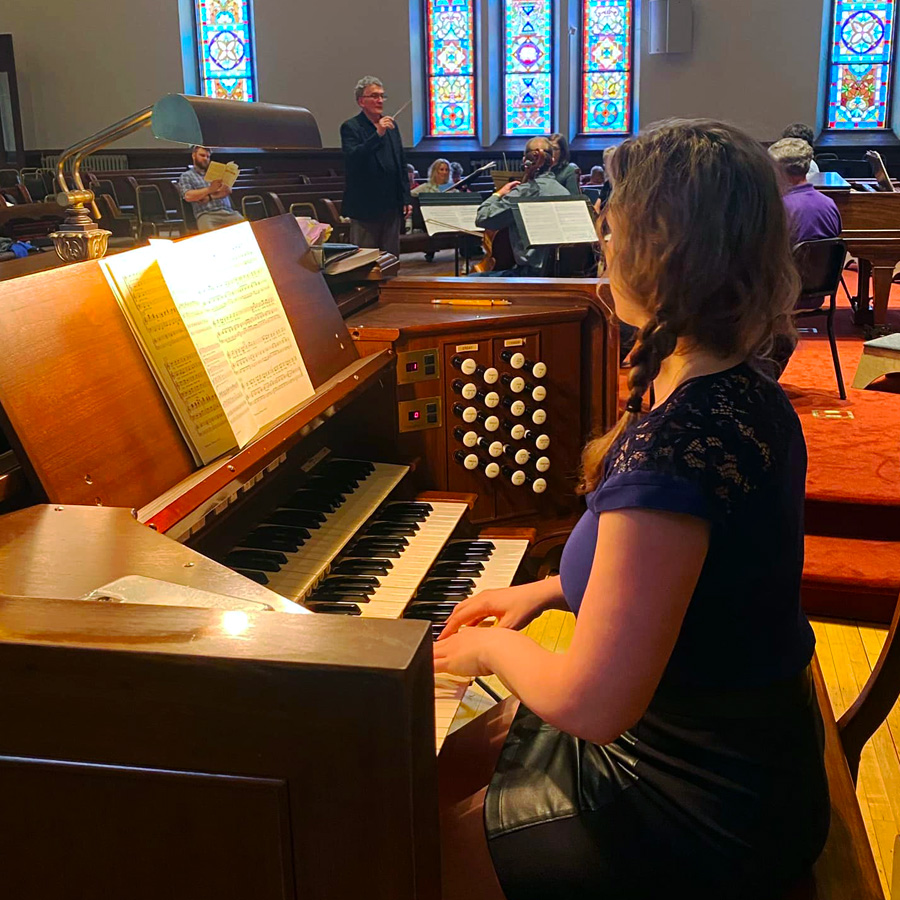Image of organ player with chamber orchestra and conductor in the background at Cappella Performing Arts Center during a rehearsal.