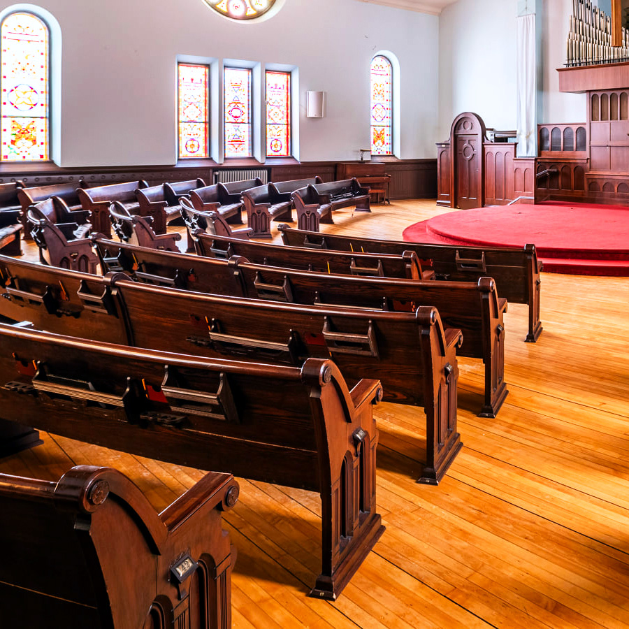 Image of Cappella Performing Arts Center Sanctuary Stage featuring the historic stained glass windows and church pew seating.