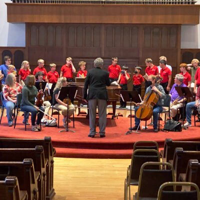 La Crosse Boychoir singing during a rehearsal at Cappella Performing Arts Center behind an accompanying chamber orchestra.